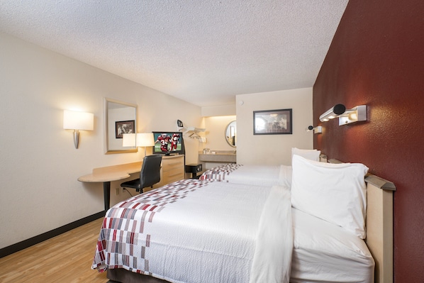 Une chambre d’hôtel avec deux lits, un bureau, une chaise, un miroir et des lampes fixées au mur.