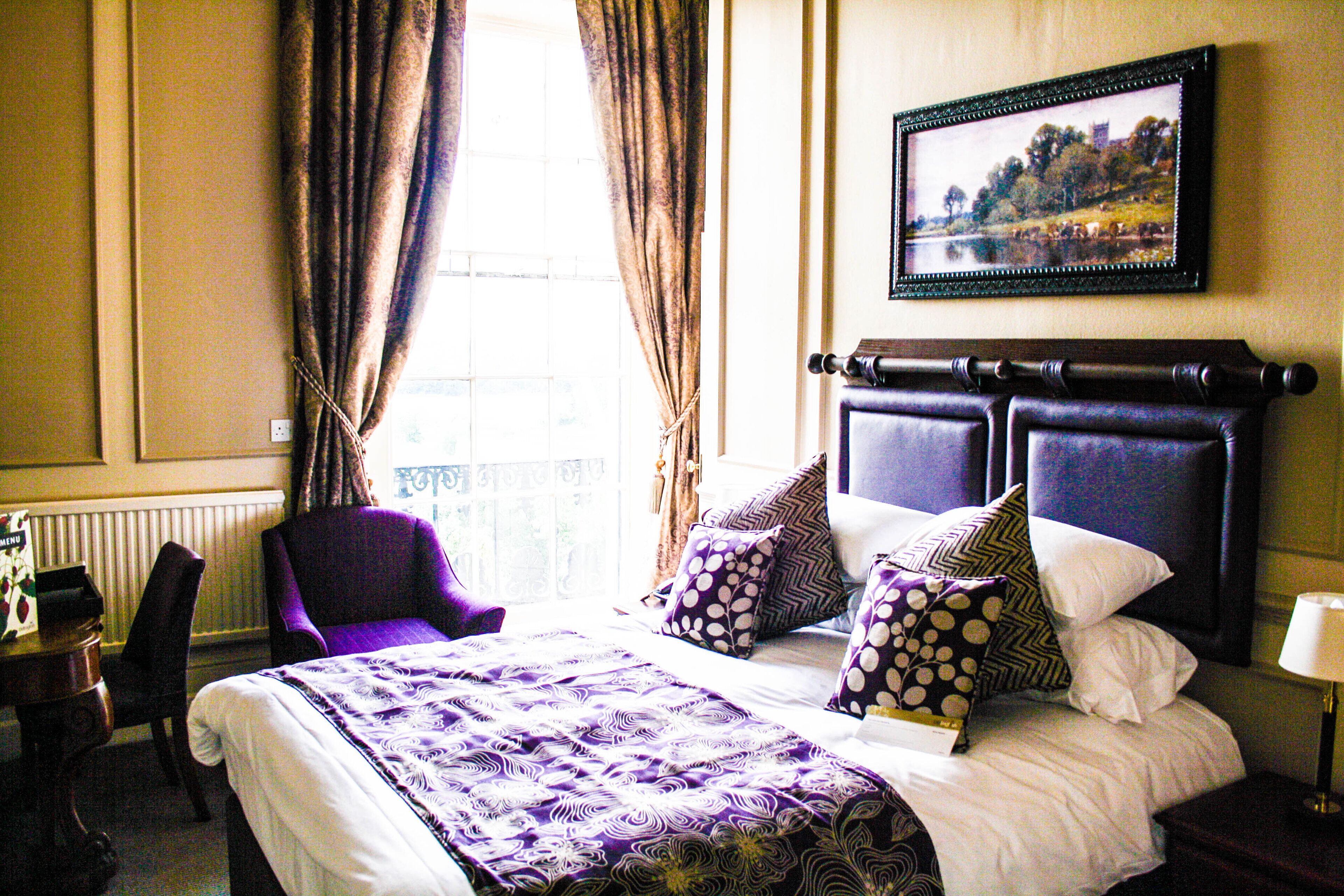 A hotel room with a large bed, a chair, a desk, and a window with curtains.