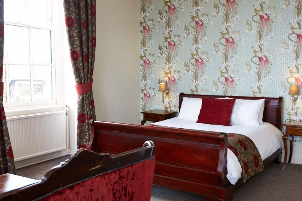 Een slaapkamer met een houten bed, bloemenbehang en twee bedlampjes.