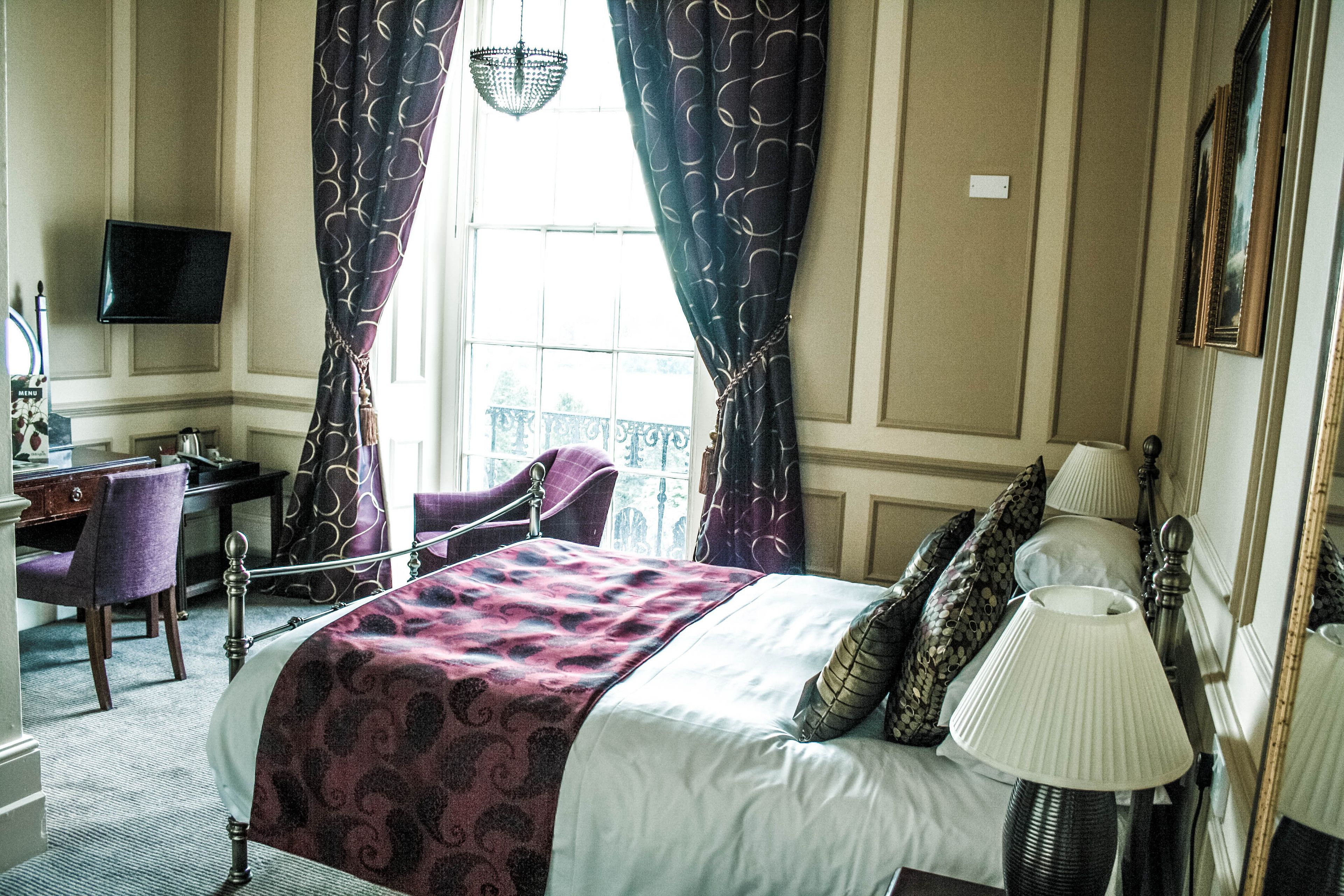 A hotel room with a bed, a desk, a chair, a TV, and a window with curtains.