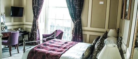 A hotel room with a bed, a desk, a chair, a TV, and a window with curtains.