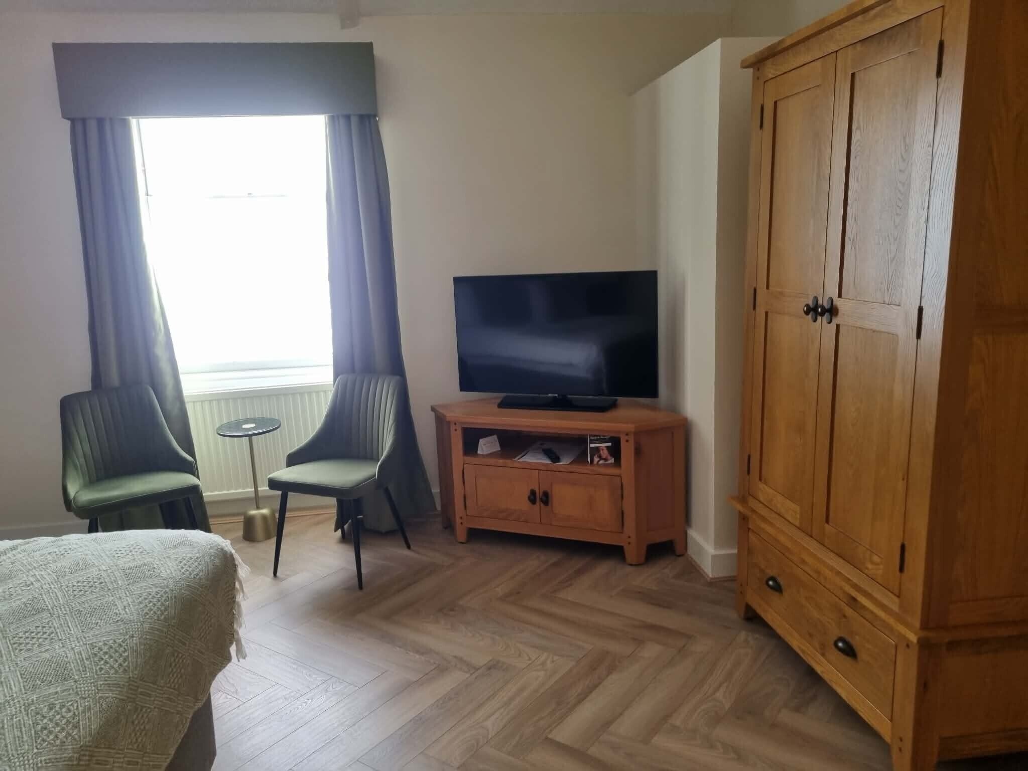 A room with a television on a wooden cabinet, two chairs, a small table, and a large wardrobe.