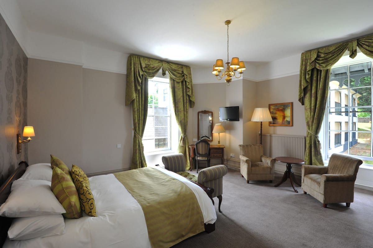 Een hotelkamer met een bed, twee fauteuils, een kleine tafel, een televisie en een raam met gordijnen.