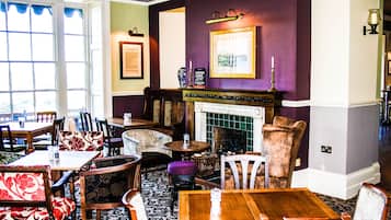 A cozy restaurant interior with wooden tables and chairs, a fireplace, and framed artwork on the walls.