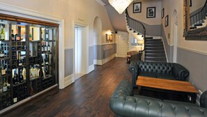 A grand staircase with a chandelier, a wine cellar, and a leather sofa in a spacious hallway.