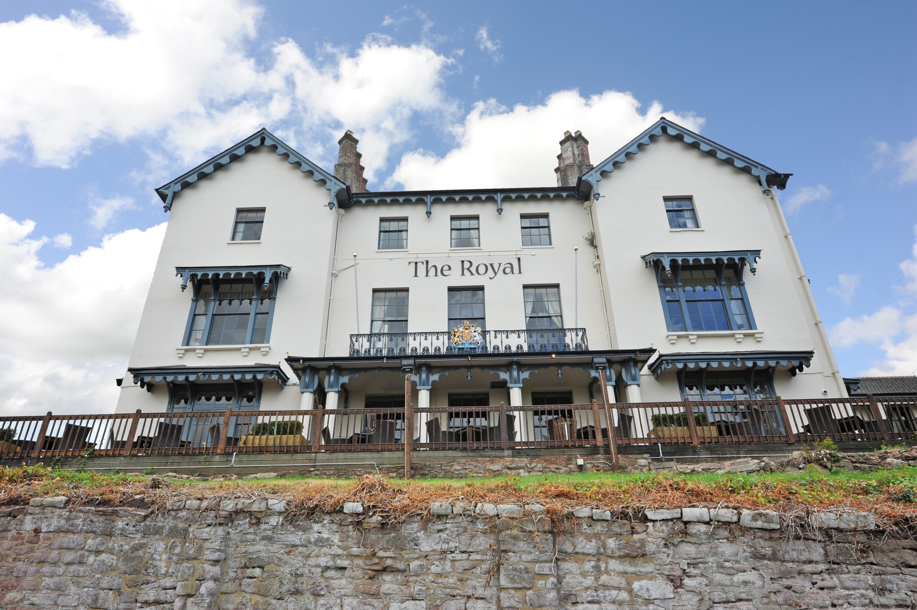 A large, white building with the name "The Royal" on the facade, featuring a balcony with railings and a stone wall in the foreground.