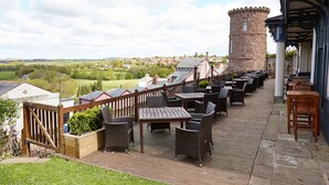 A deck with outdoor seating, a stone tower, and a view of the countryside.