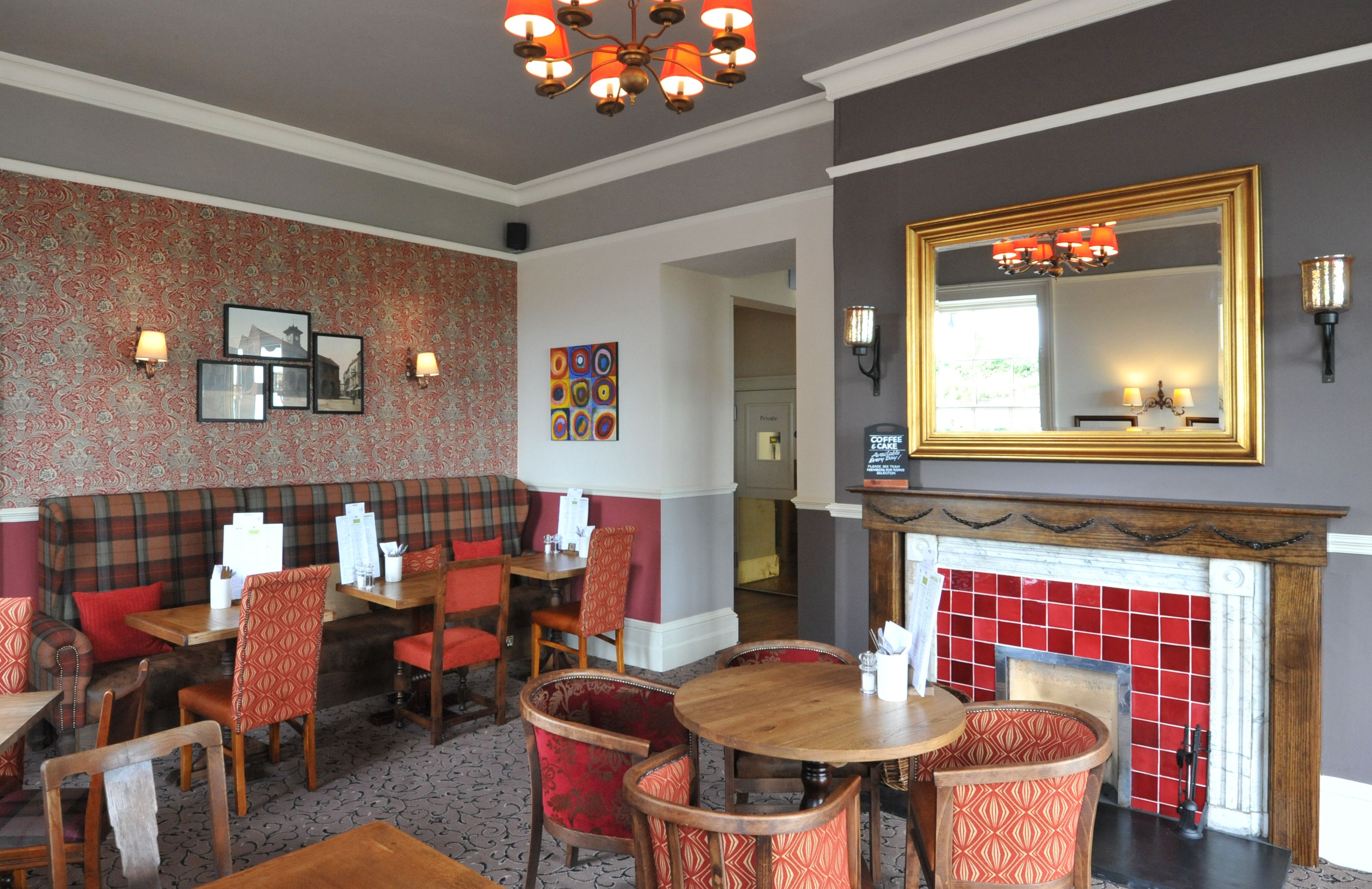 Un restaurante con chimenea, paredes con un estampado rojo y negro, y un espejo grande arriba.