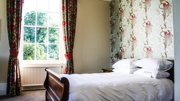Een slaapkamer met een groot raam, een bed met wit beddengoed en bloemenbehang.