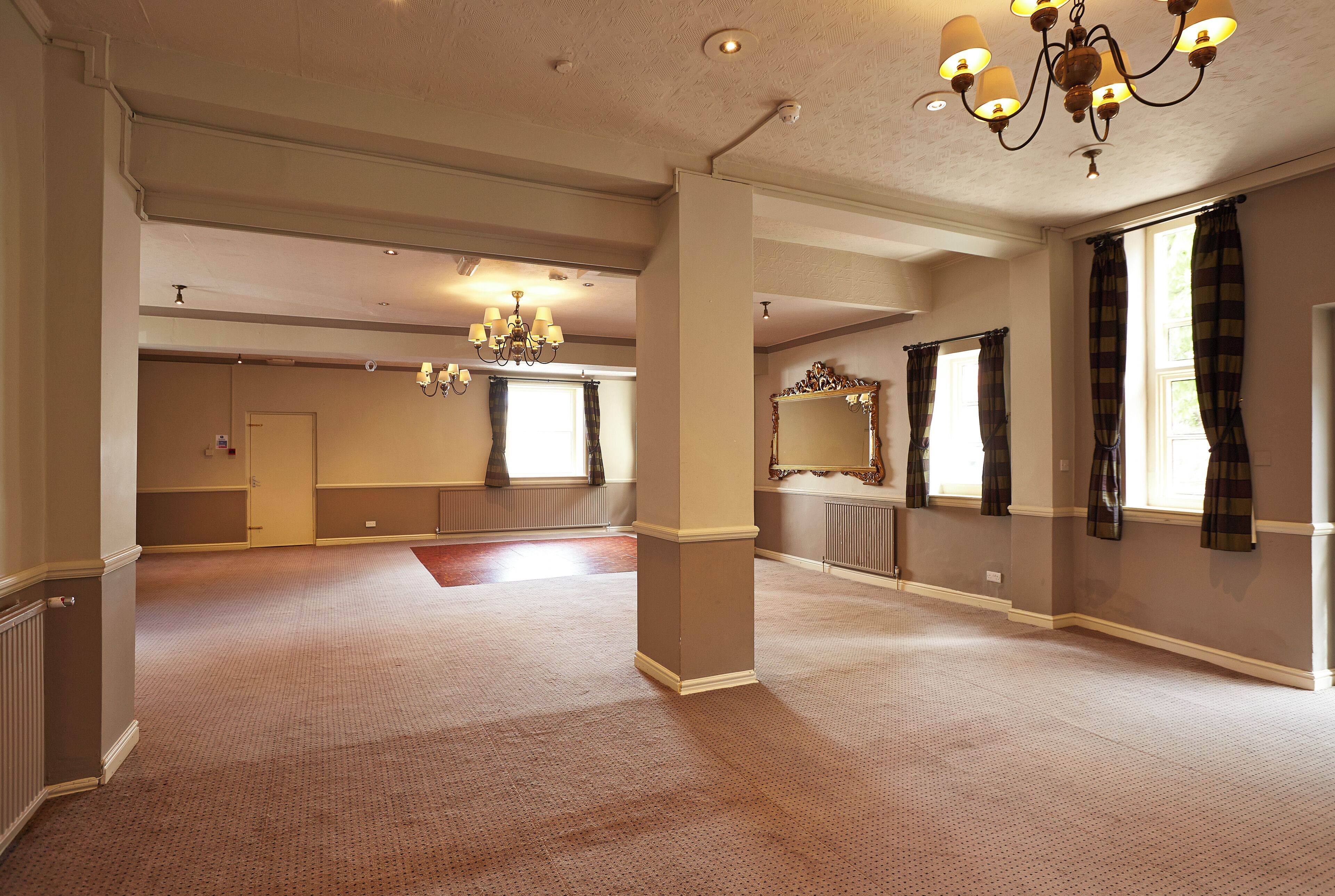 Una habitación de hotel amplia con una gran área alfombrada, un candelabro y un espejo grande.