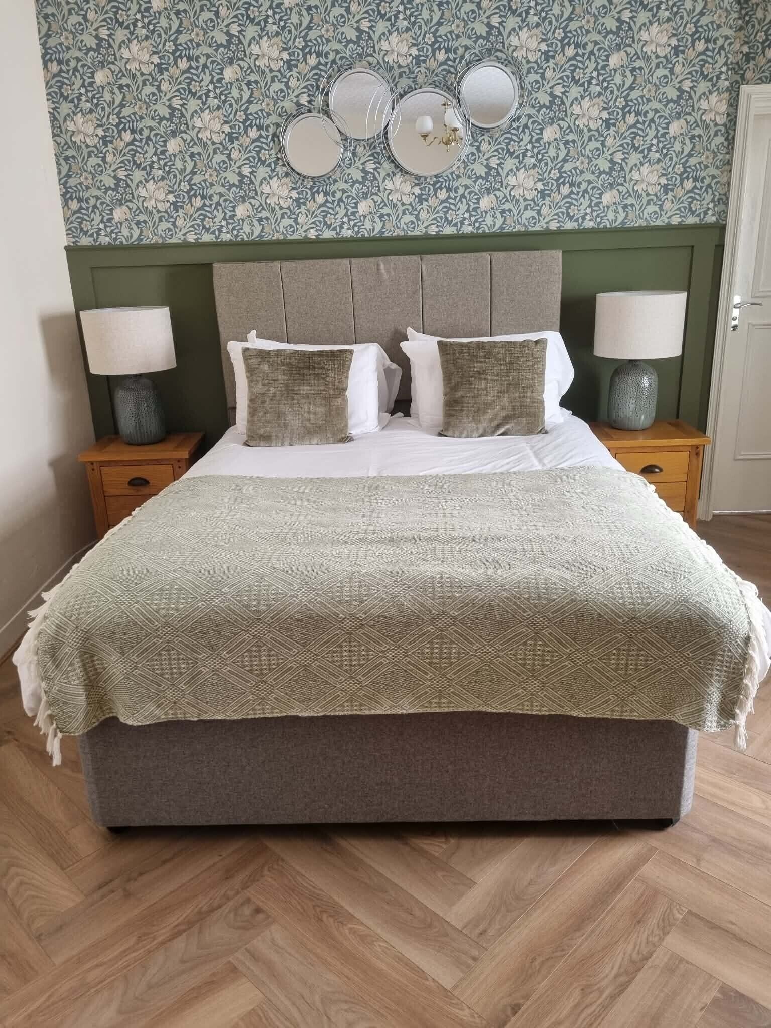 A bed with a patterned blanket, two bedside lamps, and a floral wallpaper.