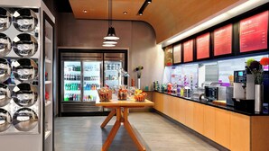 A modern cafe interior with a wooden table, a refrigerated display case, and a counter with a menu board. - Aloft by Marriott Calgary University (Calgary)