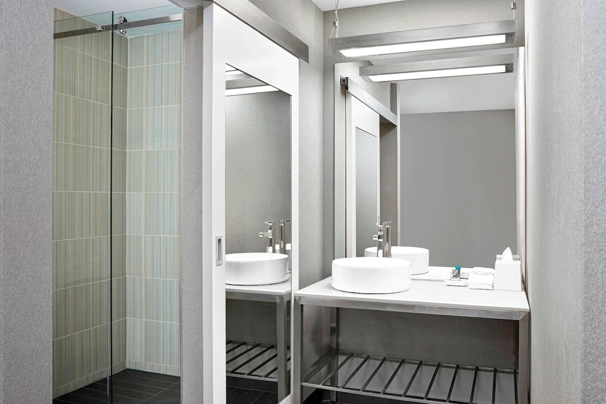 Un baño moderno con cabina de ducha de vidrio, dos lavamanos y un espejo grande.