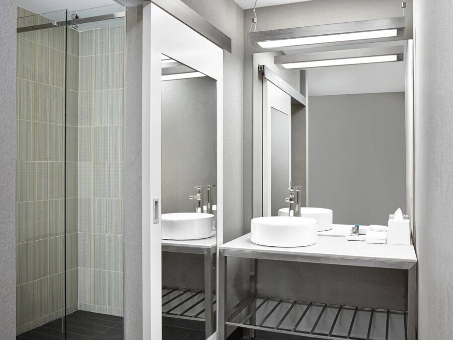 Un baño moderno con cabina de ducha de vidrio, dos lavamanos y un espejo grande.