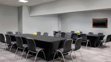 A conference room with a long table, multiple chairs, and a flat-screen TV mounted on the wall.