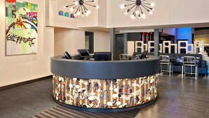 A modern reception area with a curved counter, two star-shaped ceiling lights, and a colorful abstract painting on the wall. - Aloft by Marriott Calgary University (Calgary)