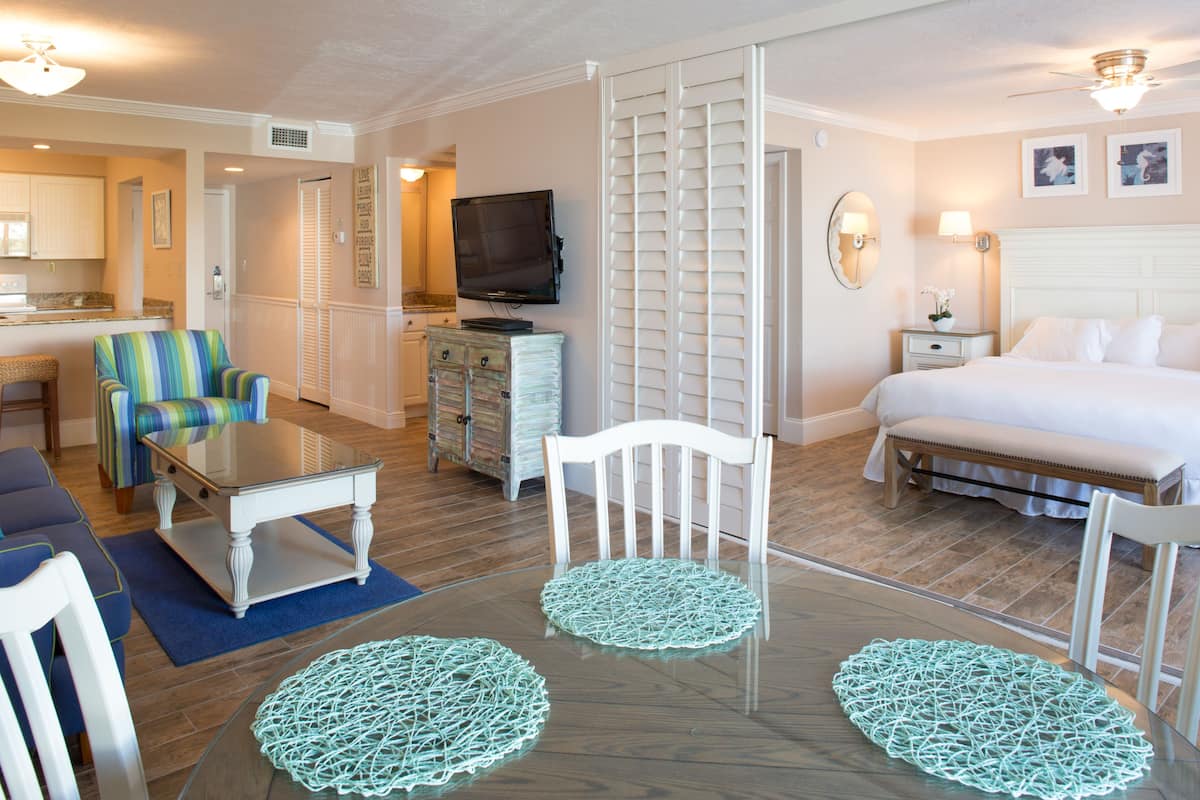 Ein Hotelzimmer mit Bett, Fernseher, Esstisch mit Stühlen, einer Couch und einer kleinen Küchenzeile.