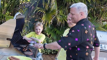A man grilling hot dogs on an outdoor grill with a child and a woman nearby.