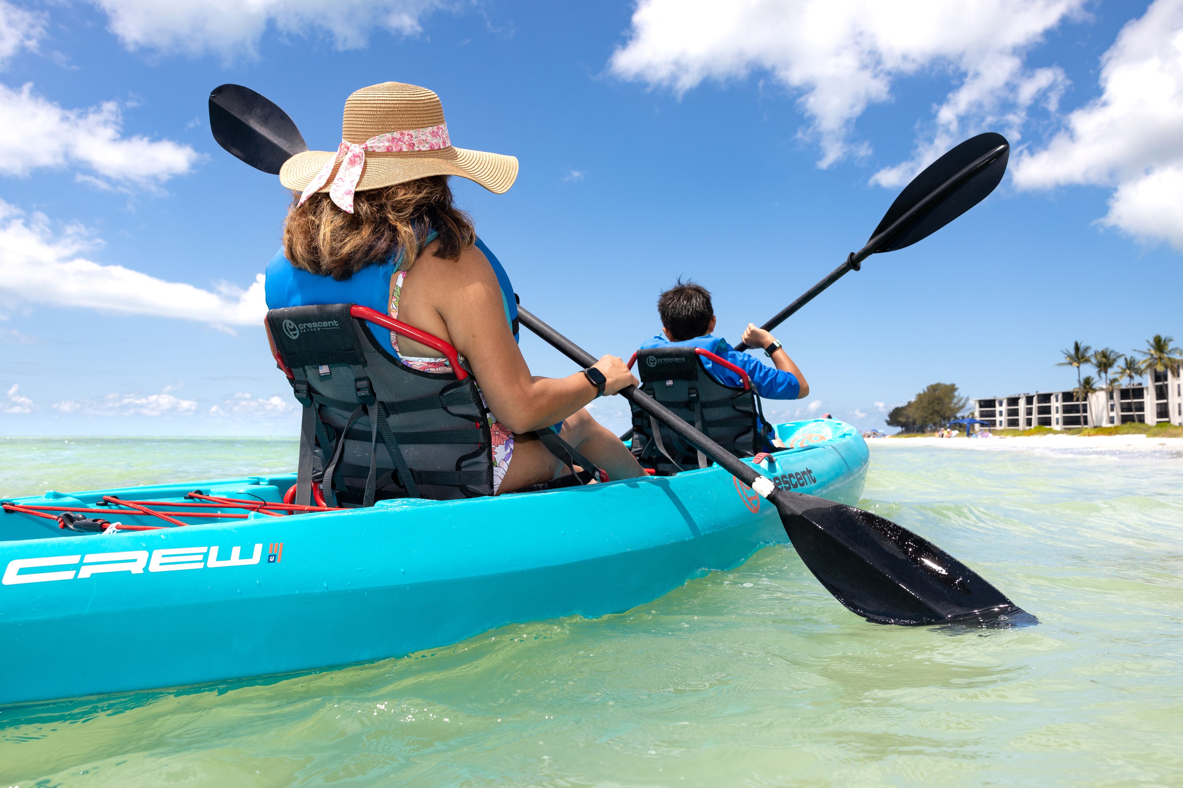 Una canoa turquesa con la palabra "CREW" en ella, manejada por una mujer y un niño.