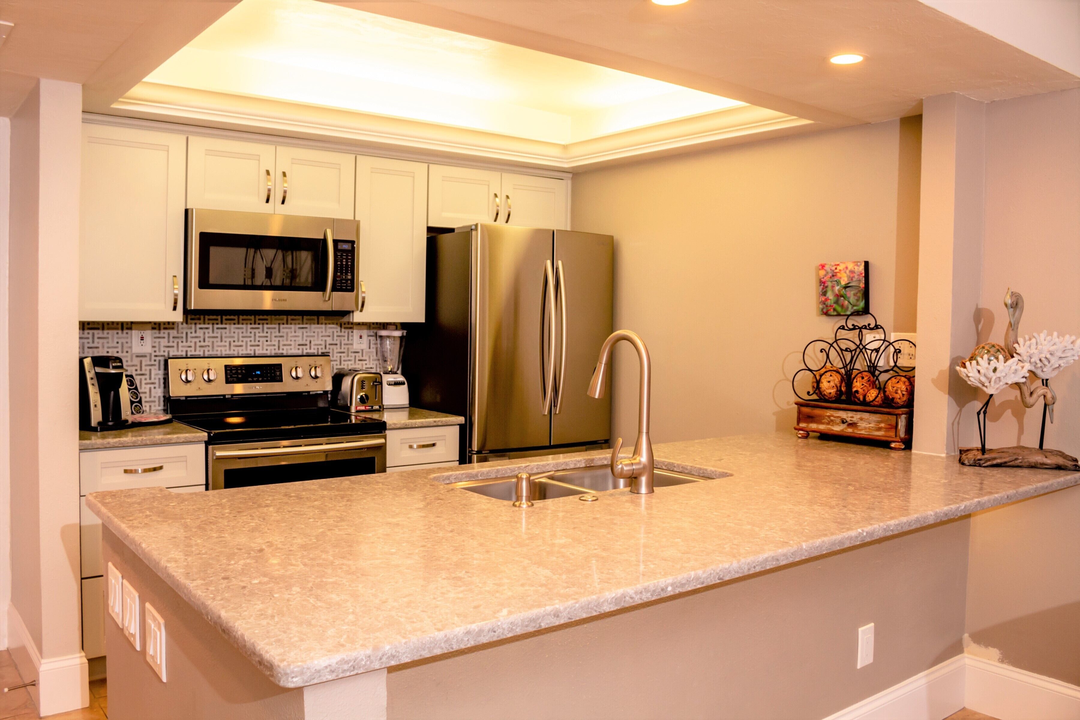 A modern kitchen with stainless steel appliances, a granite countertop, and a decorative metal rack.