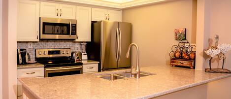 A modern kitchen with stainless steel appliances, a granite countertop, and a decorative metal rack.