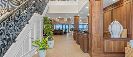 A spacious lobby with a grand staircase, wooden paneling, and potted plants.