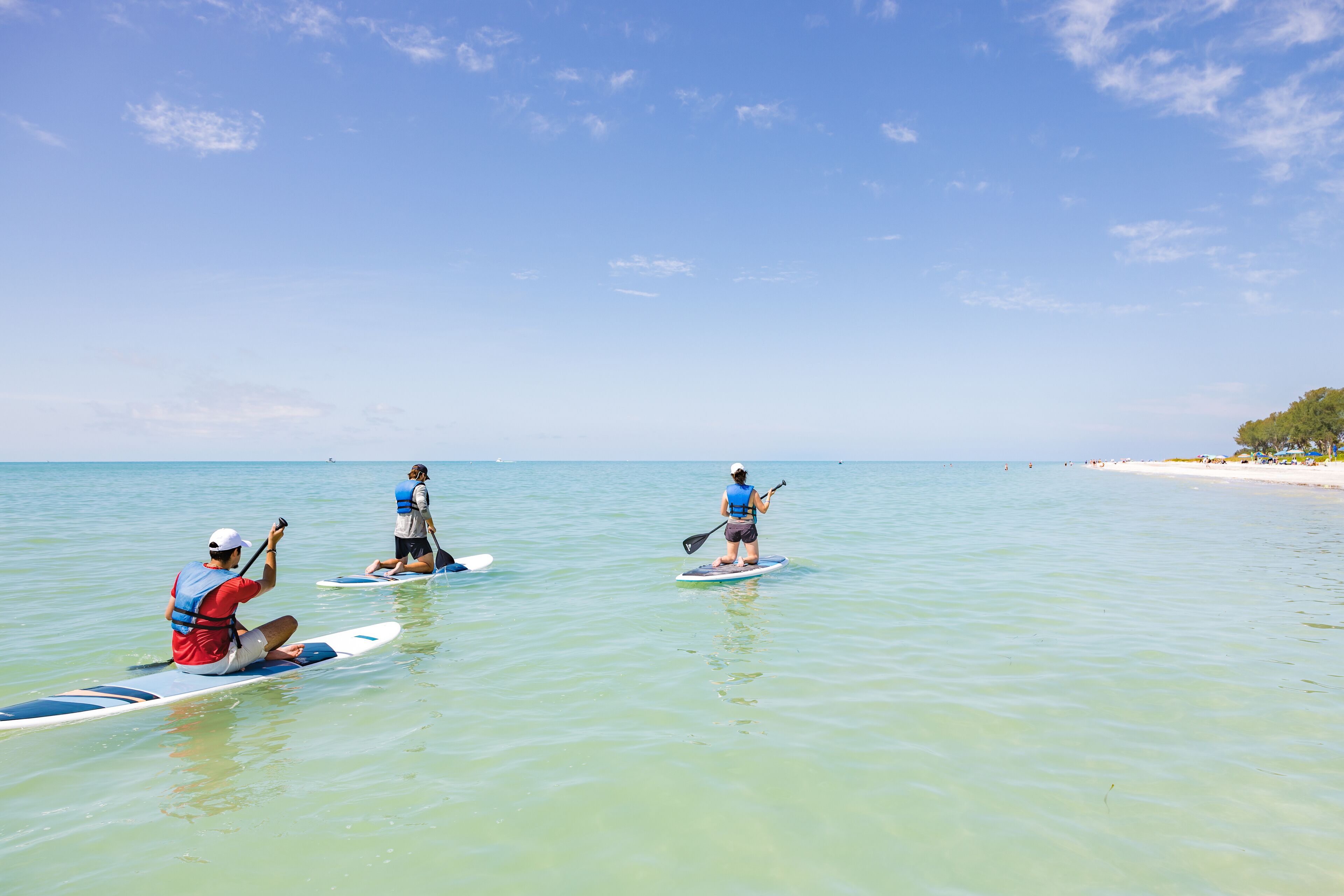 Three people paddleboarding on a calm sea with clear skies.