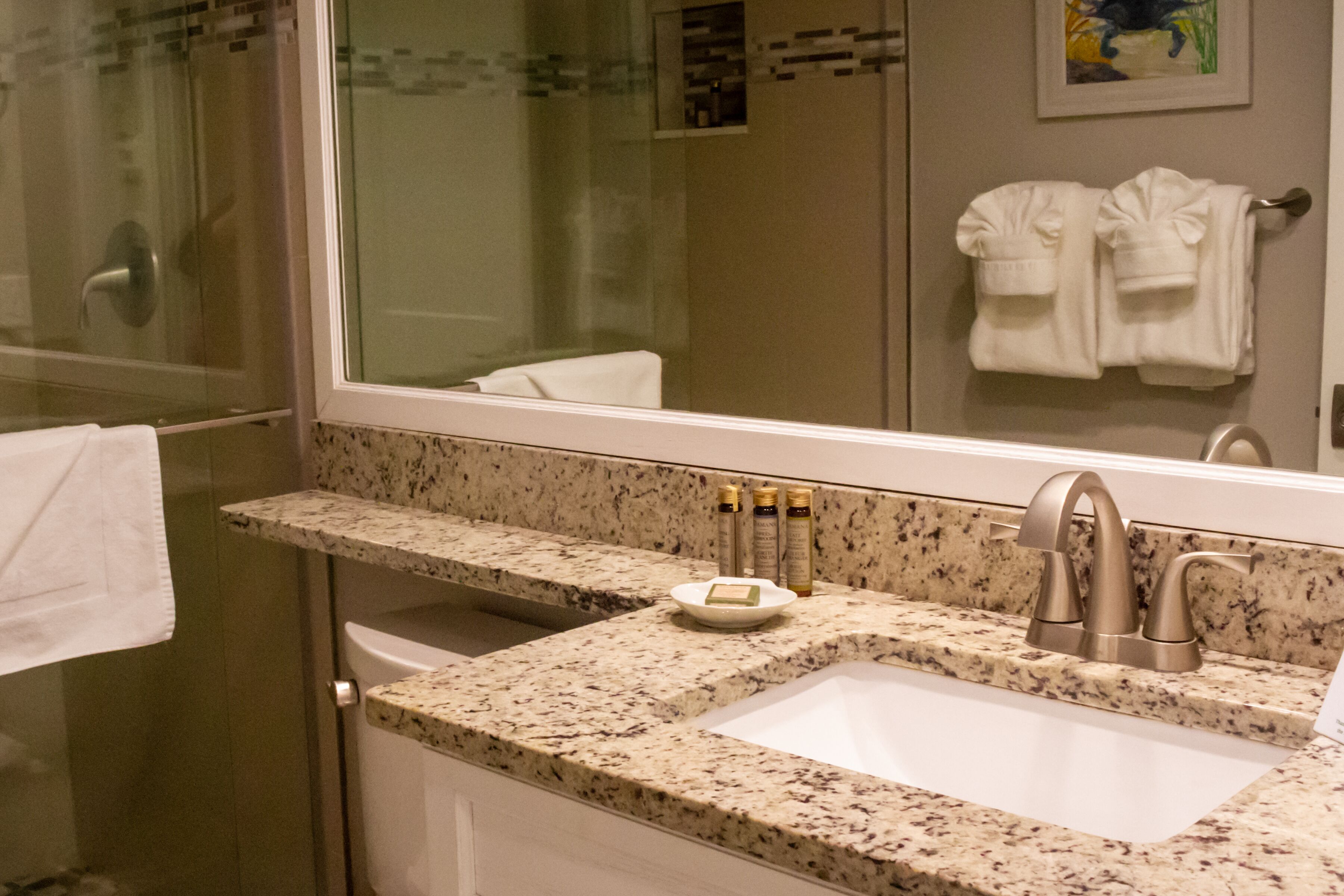 Une salle de bain dotée d’un lavabo avec un plan de toilette en granit, d’un miroir et d’une cabine de douche en verre.