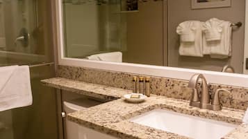 A bathroom with a granite countertop sink, a mirror, and a glass shower enclosure.