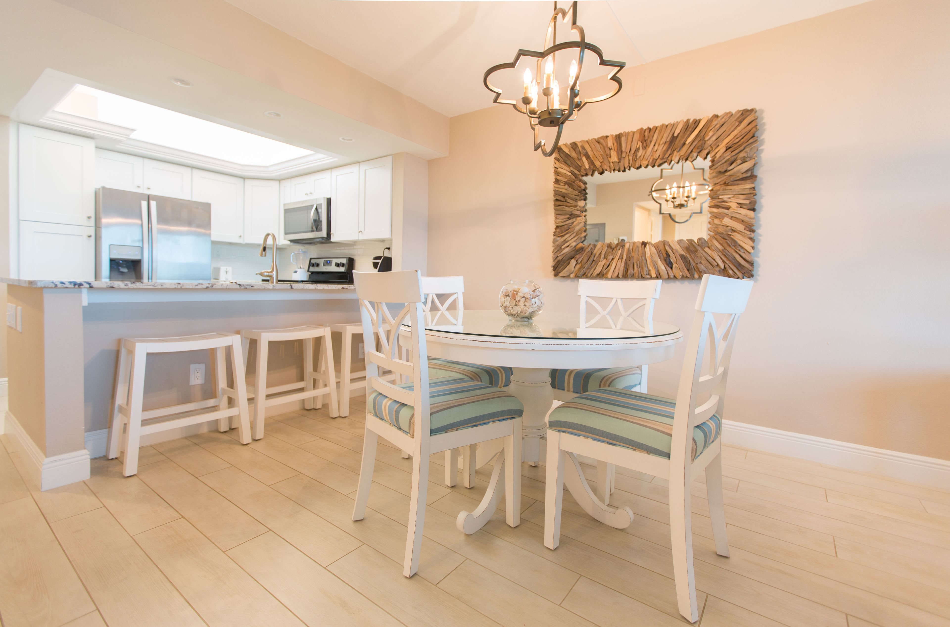 A modern kitchen with white cabinetry, a central island, and a dining area with striped chairs and a glass table.