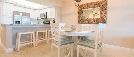 A modern kitchen with white cabinetry, a central island, and a dining area with striped chairs and a glass table.