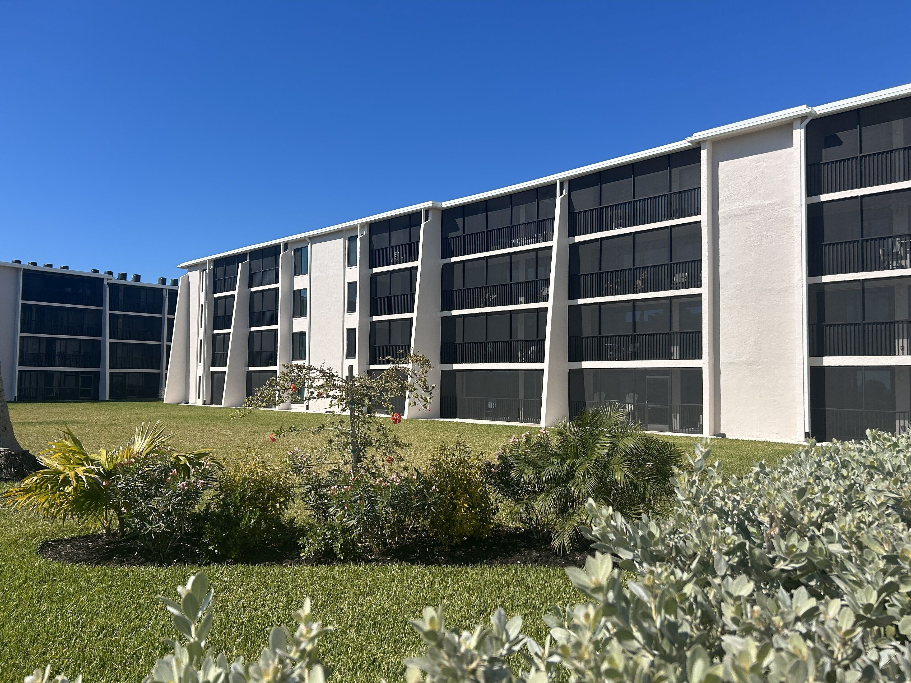 A modern building with multiple floors and large windows, surrounded by well-maintained grass and shrubs.
