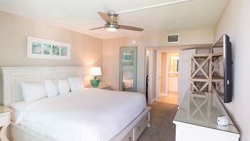 A bedroom with a large bed, a ceiling fan, a TV mounted on the wall, and a door leading to another room.