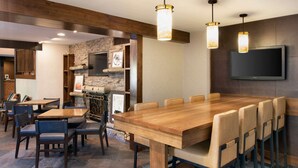 Un restaurante con una gran mesa de madera y sillas, una pared de piedra y un televisor de pantalla plana montado en la pared.