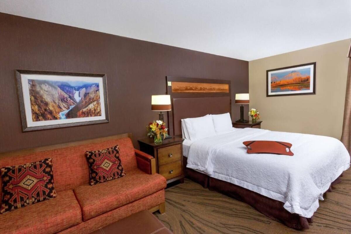 Quarto de hotel com cama, sofá, mesa de cabeceira e duas luminárias fixadas na parede.