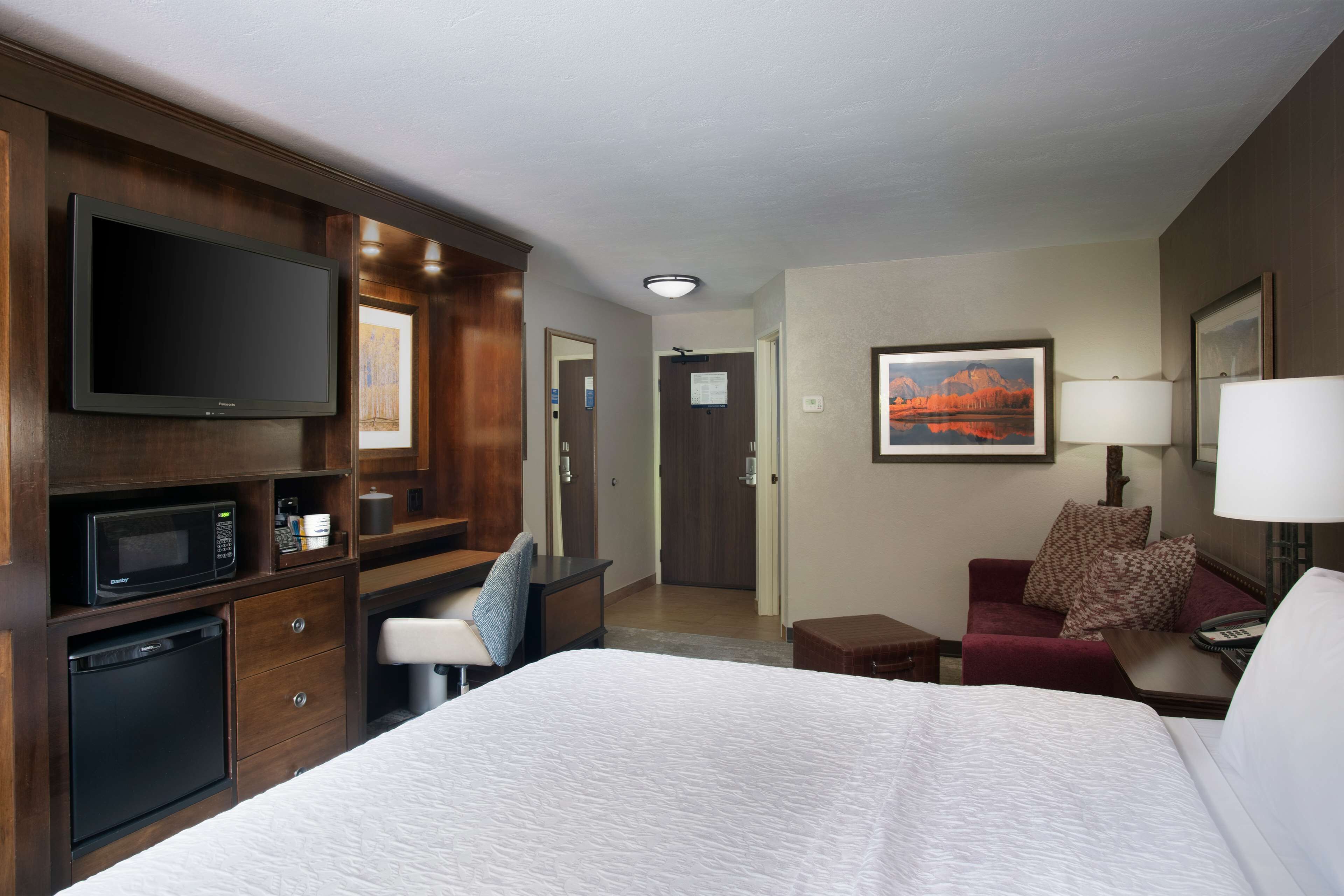 A hotel room with a bed, a desk with a computer, a microwave, and a refrigerator.