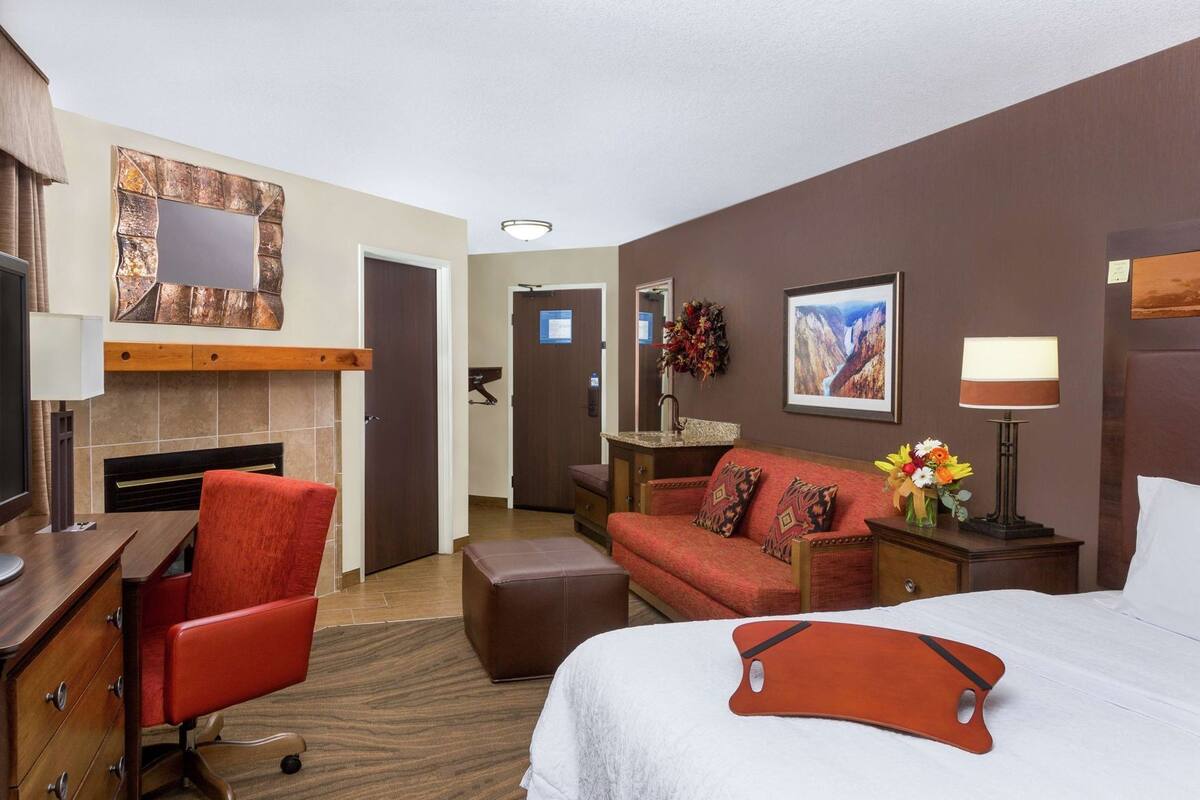 Quarto de hotel com cama, escrivaninha, poltrona, sofá, televisão, lareira e banheiro.