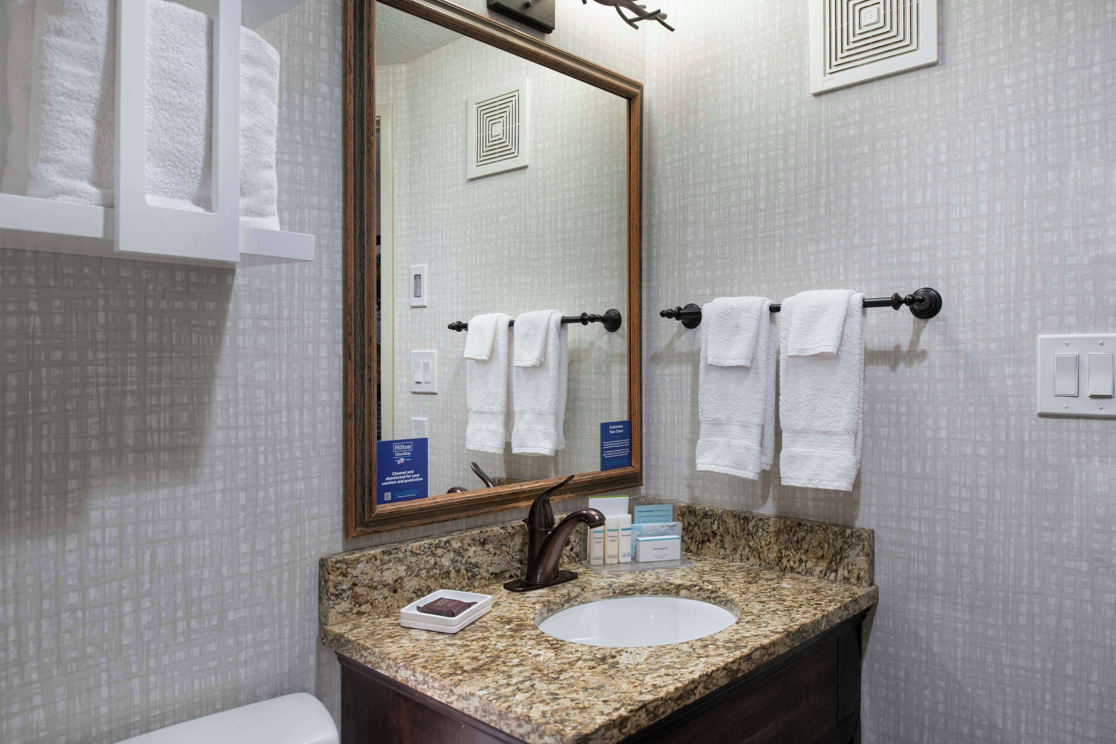 Un baño con lavamanos de encimera de granito, un espejo grande y dos toalleros con toallas blancas.