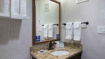 Un baño con lavamanos de encimera de granito, un espejo grande y dos toalleros con toallas blancas.