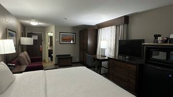 Habitación de hotel con una cama grande, un escritorio, un televisor y un microondas.