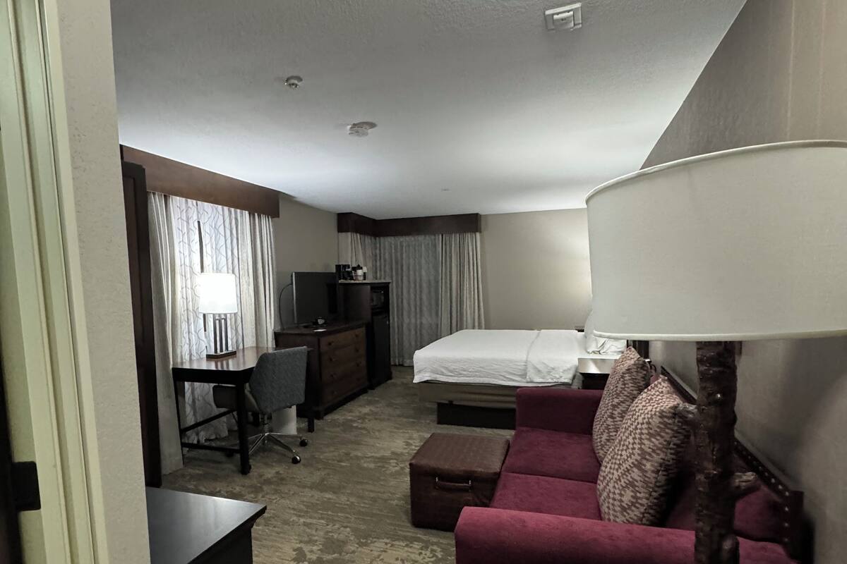 Quarto de hotel com cama, escrivaninha, cadeira, sofá, luminária e uma mesinha.