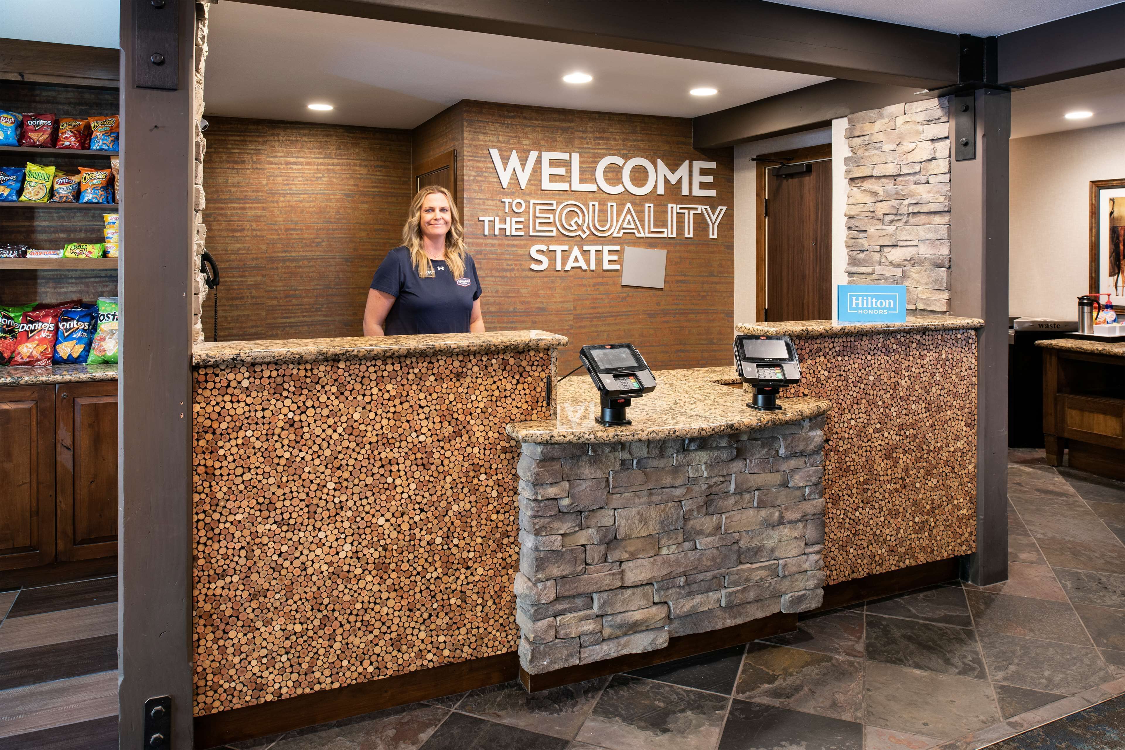 A hotel reception area with a stone and wood design, a welcome sign, and a self-service kiosk.