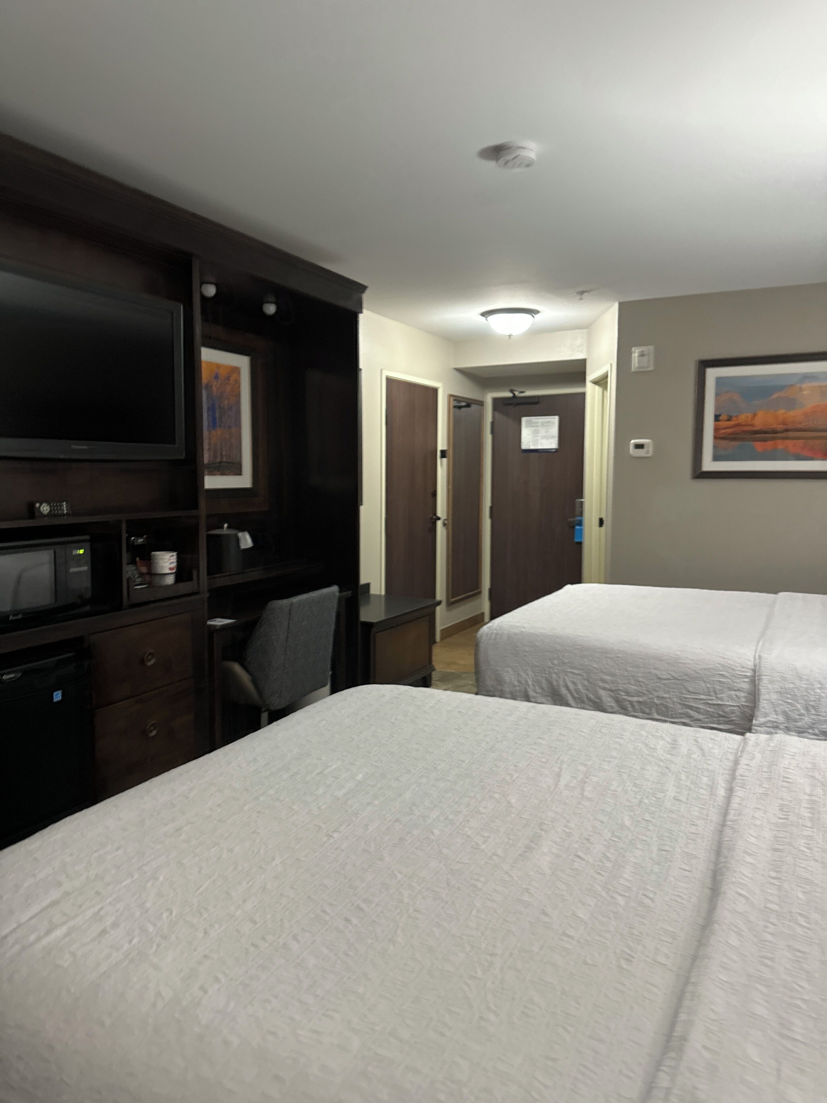 A hotel room with two beds, a desk with a computer, a television, and a microwave.