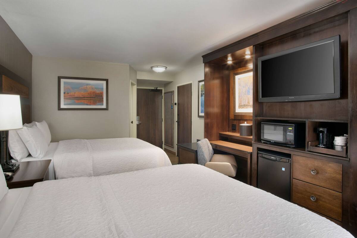 Quarto de hotel com duas camas, uma escrivaninha com computador, TV de tela plana, micro-ondas e cafeteira.