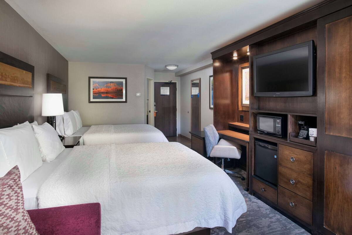 Quarto de hotel com duas camas, uma televisão, uma escrivaninha com cadeira e um micro-ondas.