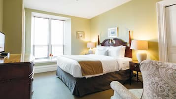 A hotel room with a large bed, two bedside lamps, a dresser, a chair, and a window with blinds.