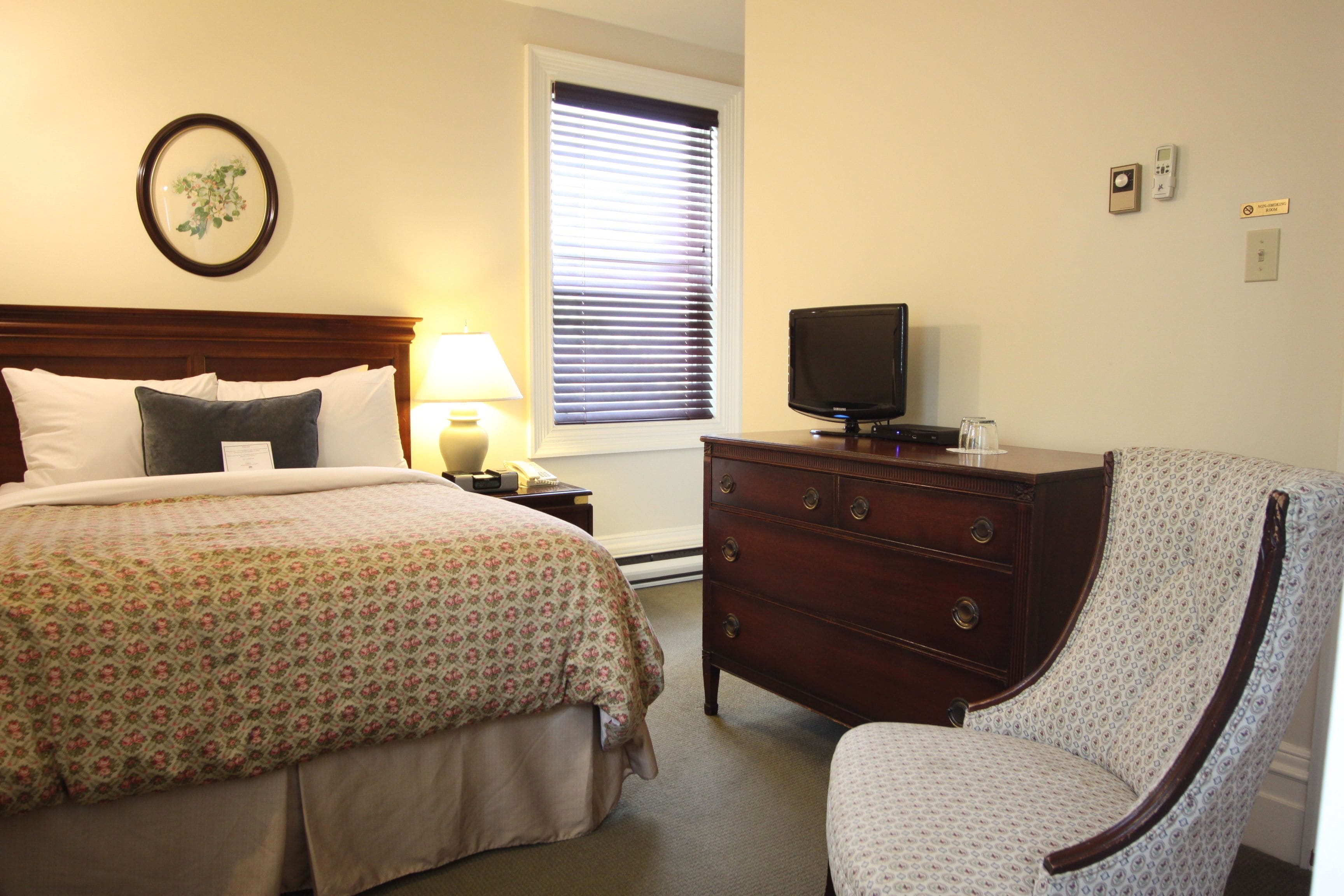 A hotel room with a bed, a dresser, a television, and a chair.
