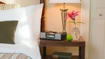 Ein ordentlich bezogenes Bett mit einem gestreiften Kopfkissen, ein Nachttisch mit Lampe, einem Radio, einem grünen Apfel, einer Vase mit einer Blume und zwei Büchern.