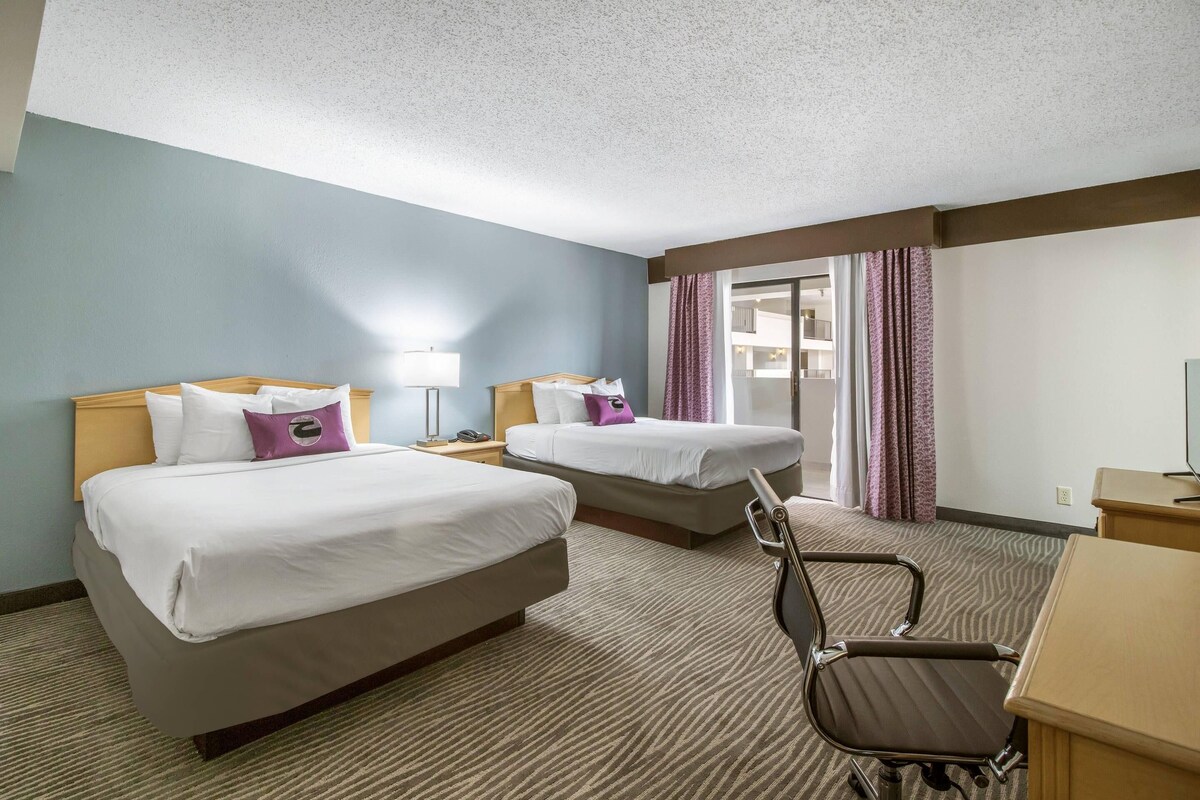 Habitación de hotel con dos camas, un escritorio, una silla y vistas al exterior.