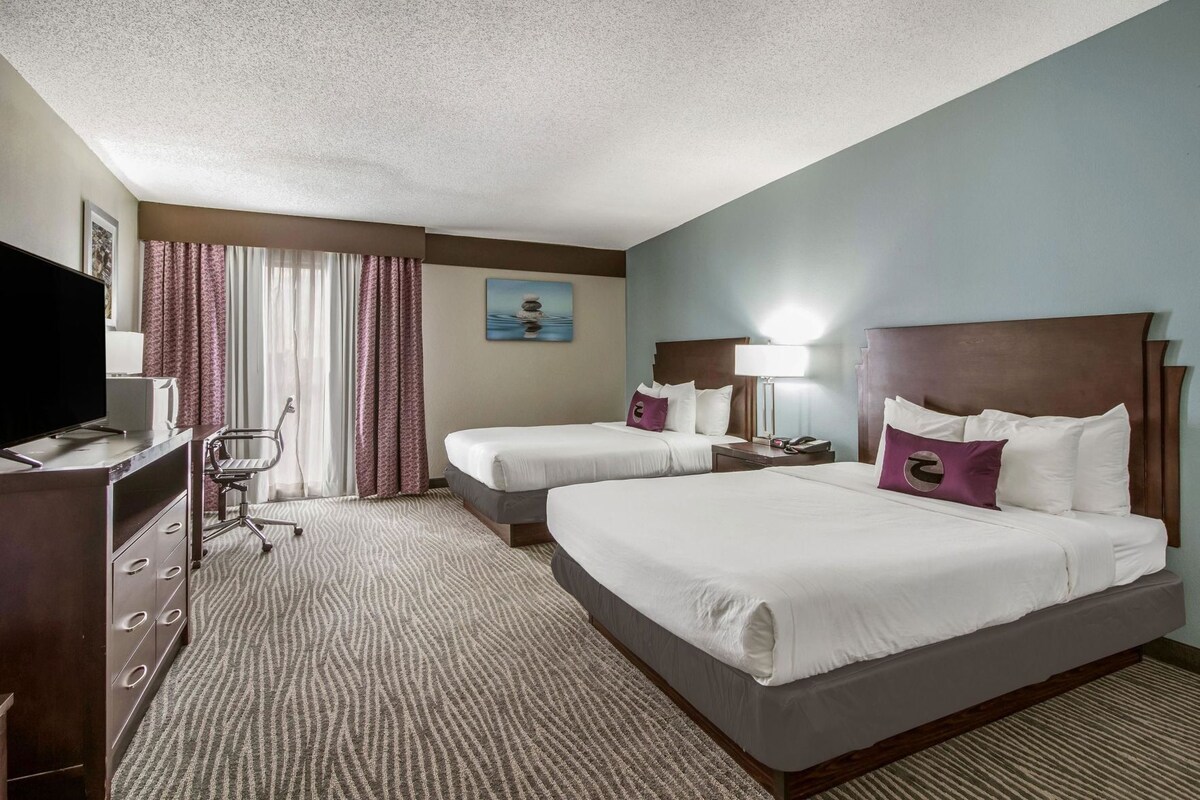 Habitación de hotel con dos camas, un escritorio, una silla, un televisor y un cuadro en la pared.